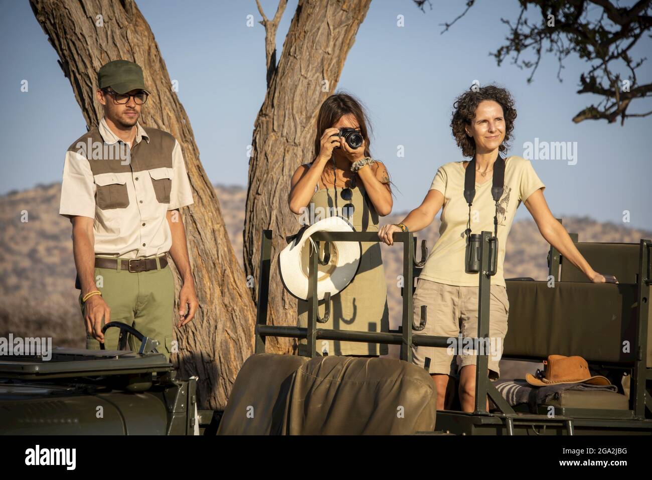 Safari guida e le donne viaggiatori in piedi in una jeep parcheggiata sotto un albero di acacia facendo una foto e guardando fuori sulla savana al gioco di Gabus R... Foto Stock