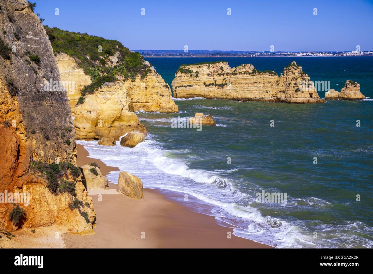 L'oceano Atlantico naviga sulla spiaggia di Dona Ana con la sua costa rocciosa di arenaria e le cataste di mare lungo la famosa costa dell'Algarve Foto Stock