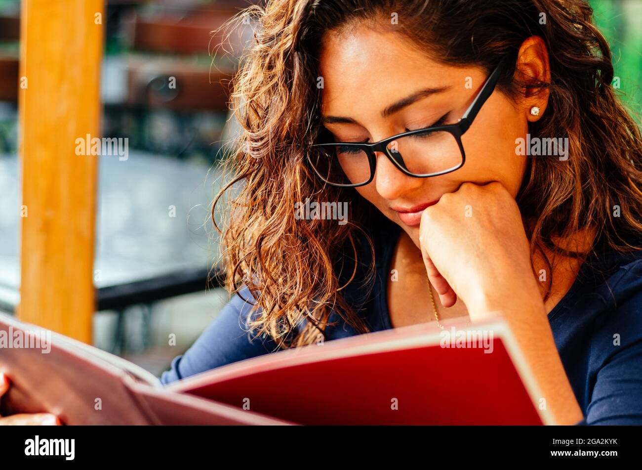 Bella, giovane donna seduta nel parco verde leggere un libro con gli occhiali, sorridente. Foto Stock