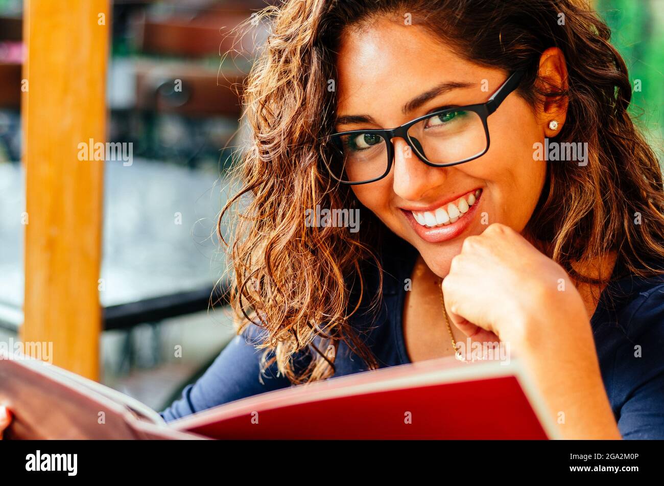 Bella, giovane donna seduta nel parco verde leggere un libro con gli occhiali, sorridente. Foto Stock