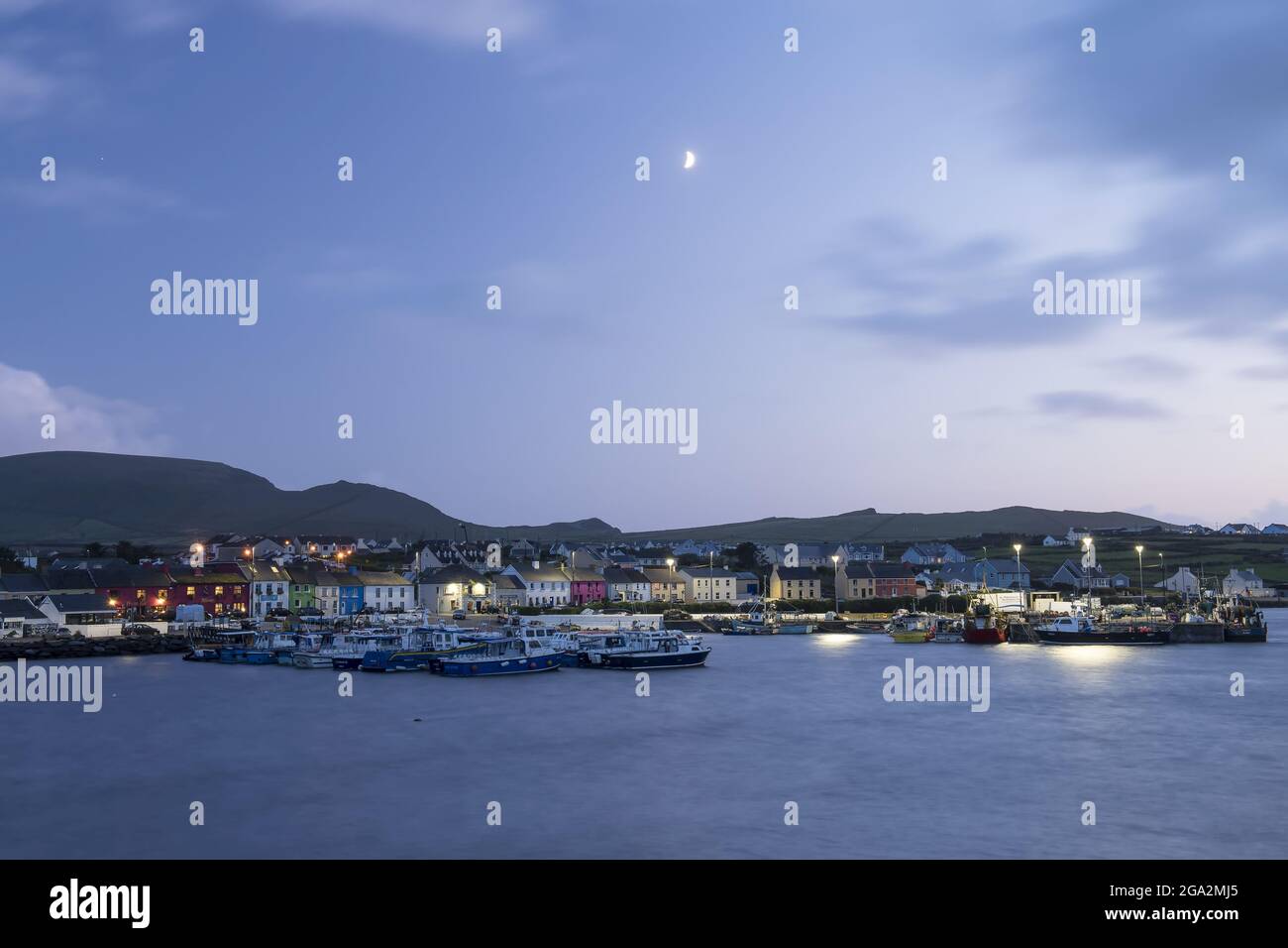 La piccola città di Portmagee e porto al crepuscolo con il quarto di luna nel cielo; Portmagee, Contea di Kerry, Irlanda Foto Stock