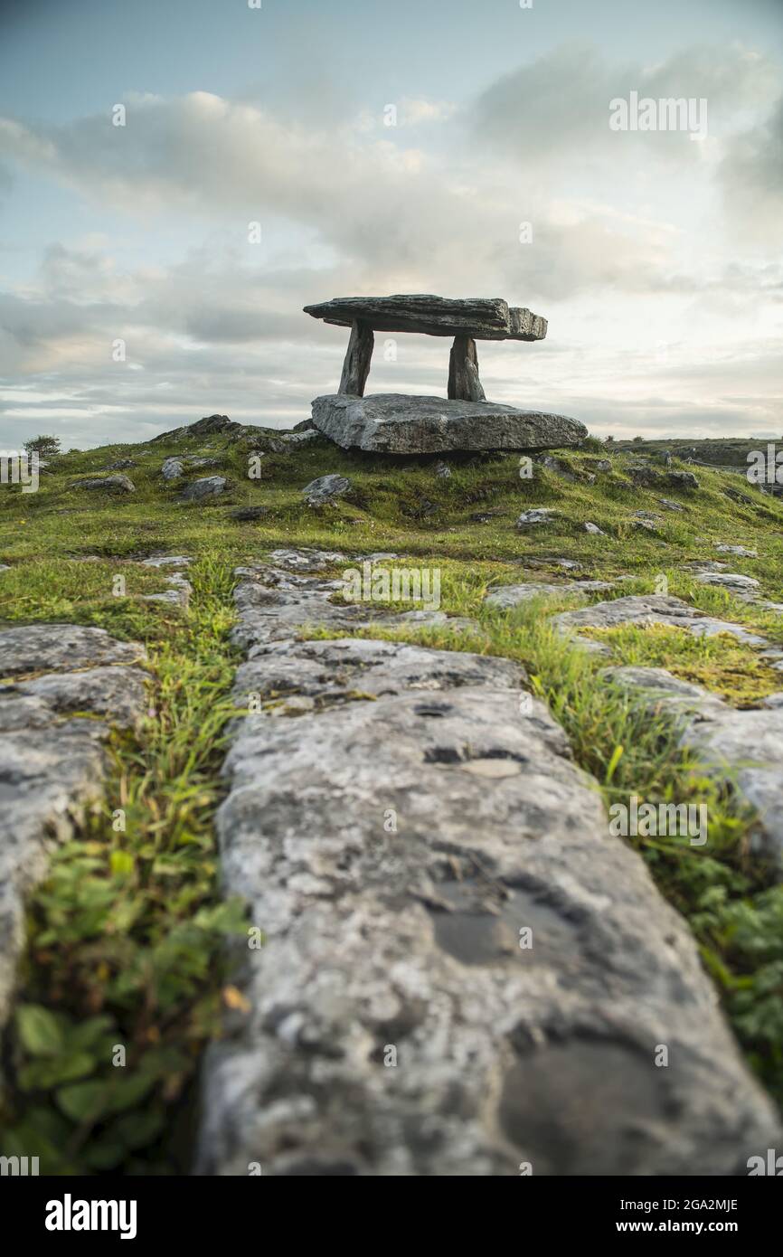 Il paesaggio carsico roccioso che porta alla tomba portale del Dolmen Poulnabrone con una nuvolosa sul Burren all'alba; County Clare, Irlanda Foto Stock