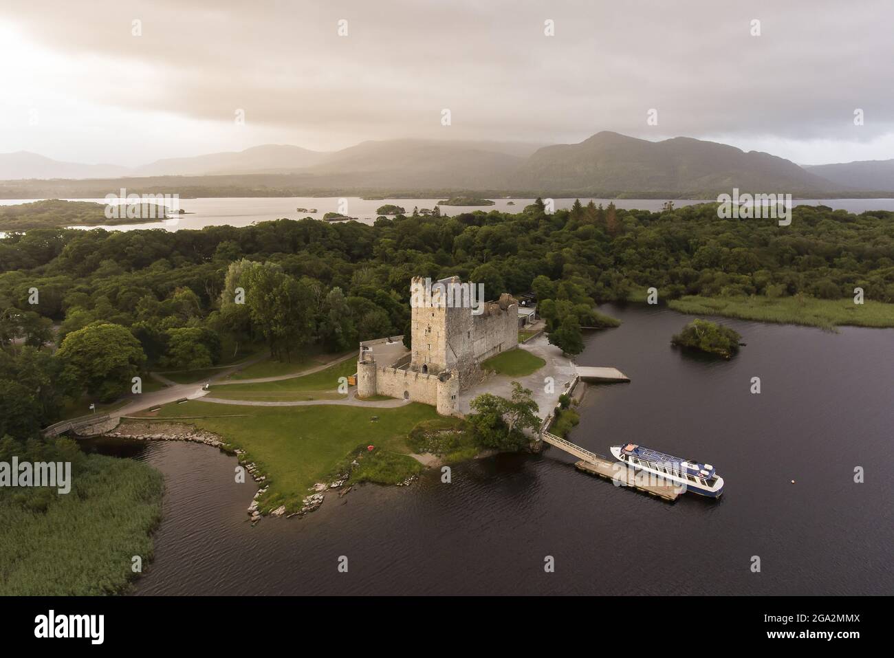 Vista aerea del Castello di Ross su un'insenatura di Lough Leane con un cielo grigio e misteriosa e montagne sullo sfondo del Parco Nazionale di Killarney Foto Stock