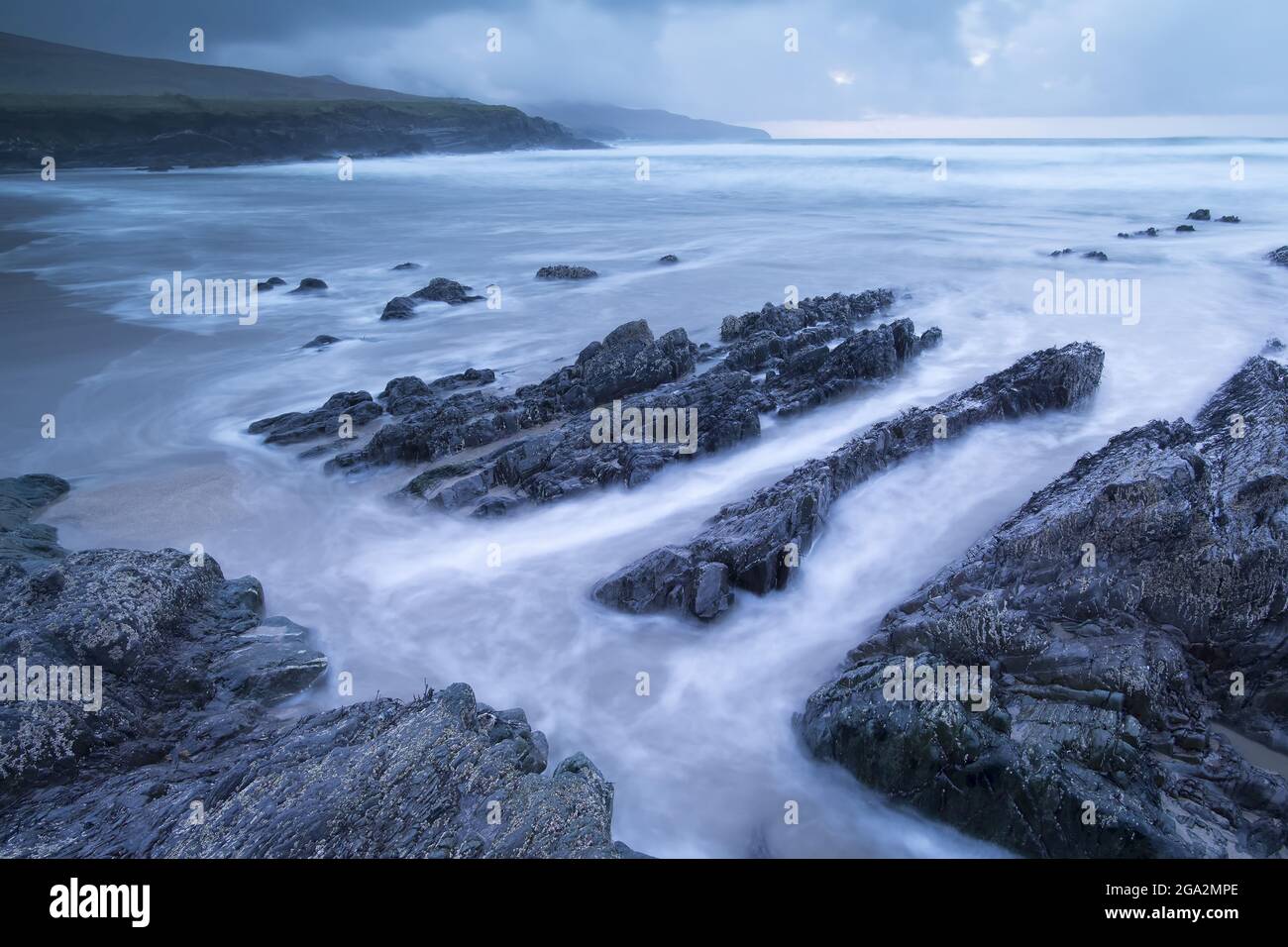 Ripiano roccioso sulla spiaggia con un cielo tempestoso a St Finian's Bay (The Glen) sull'Oceano Atlantico lungo lo Skellig Ring; County Kerry, Irlanda Foto Stock