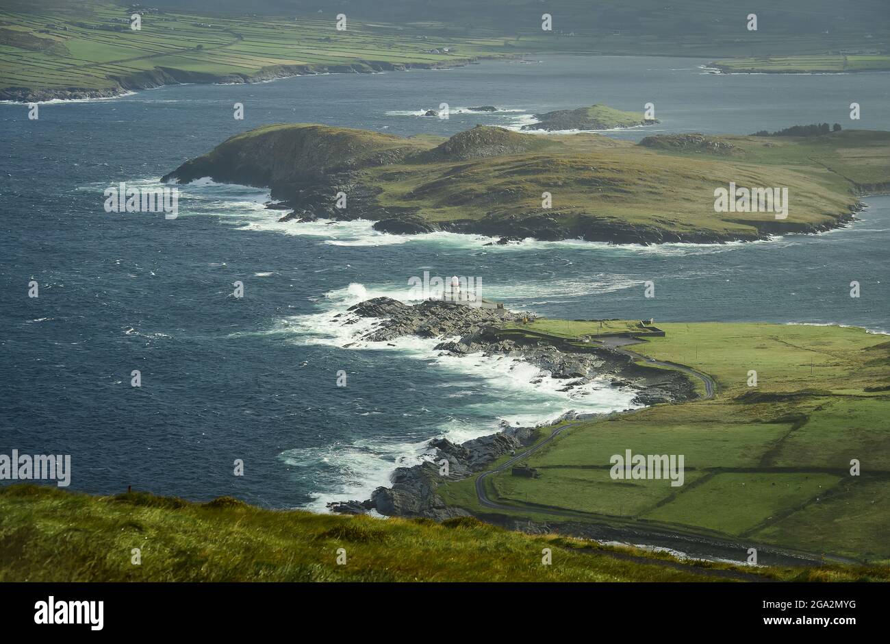 Vista aerea delle onde che si infrangono lungo la costa frastagliata di Valentia in una giornata di sole con il faro di Valentia Island a Cromwell Point, costruito su... Foto Stock