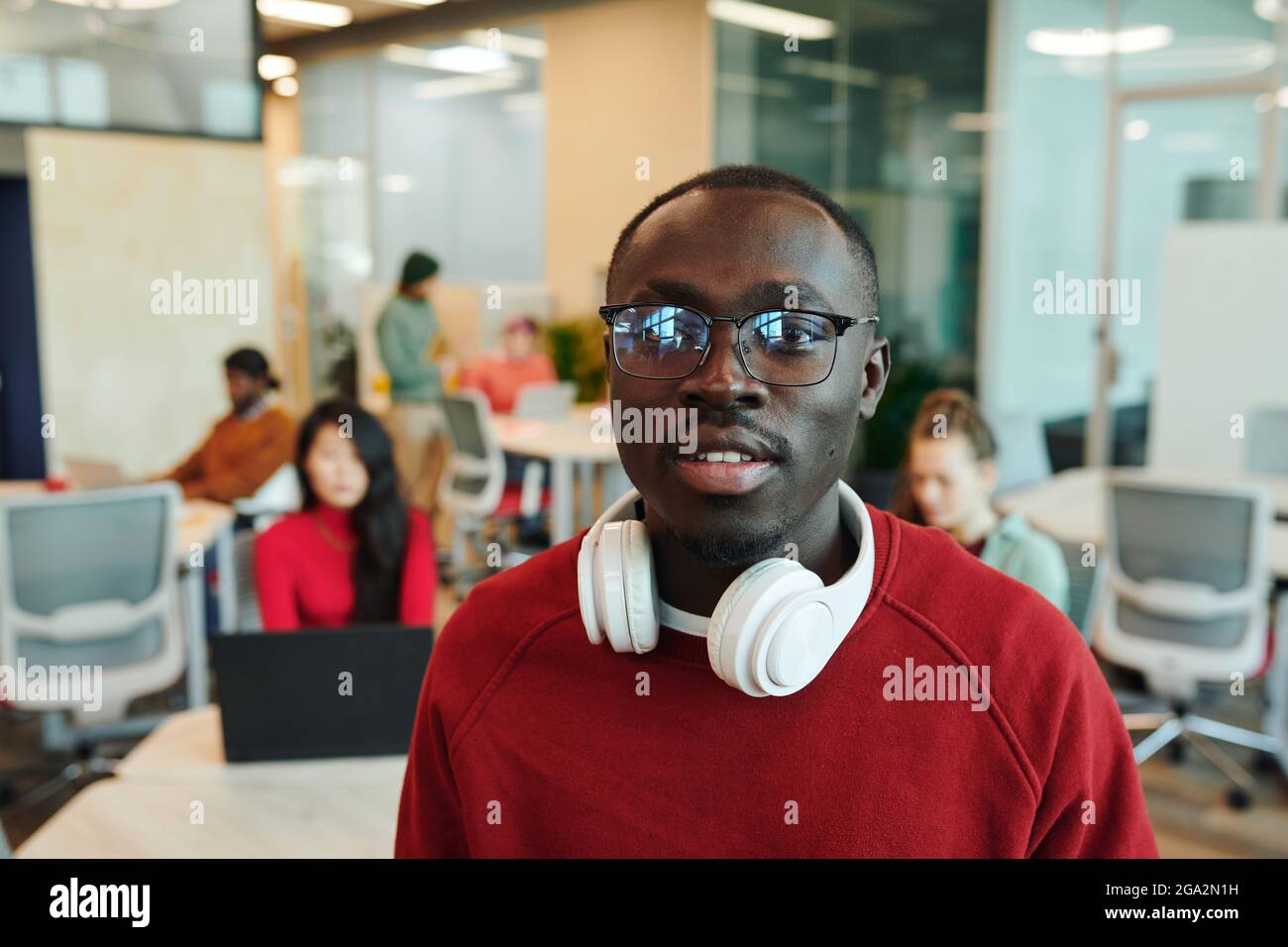 Giovane uomo d'affari serio o designer di etnia africana che tiene smartphone quando si parla con il cliente in un ambiente di lavoro Foto Stock