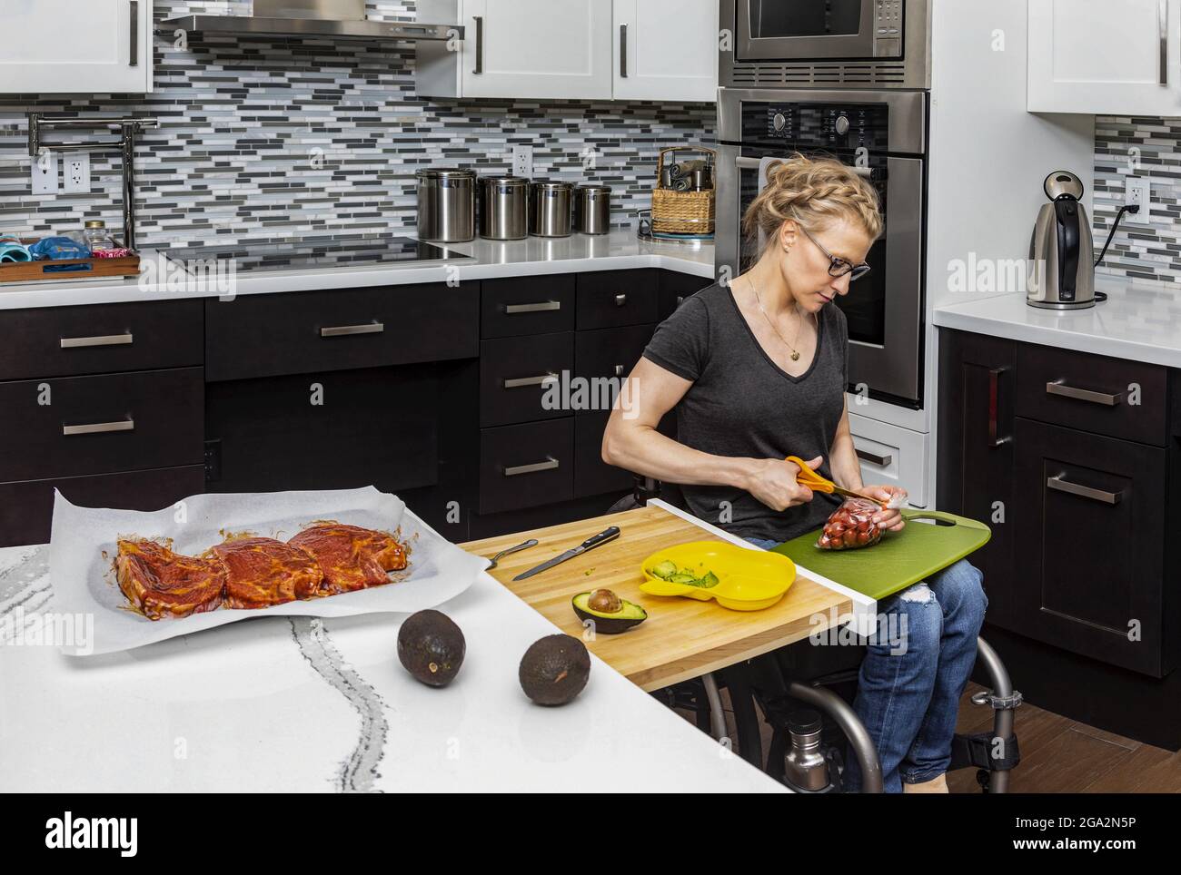 Una donna paraplegica che prepara un pasto per la sua famiglia in cucina mentre lavora da una sedia a rotelle; Edmonton, Alberta, Canada Foto Stock