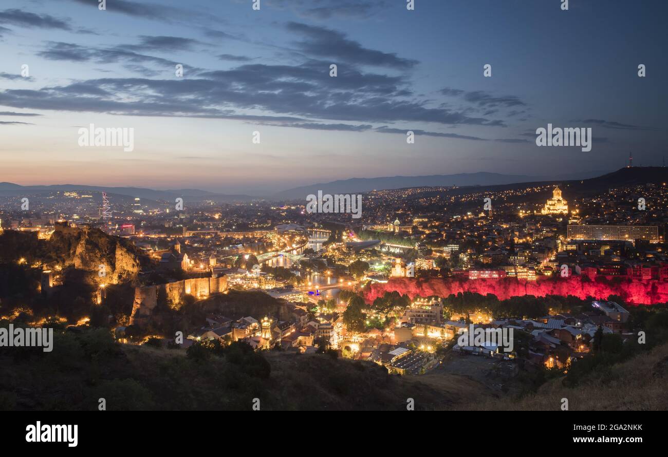 Crepuscolo cade sulla capitale di Tbilisi con le sue luci della città che mettono in risalto la Cattedrale della Santissima Trinità di Tbilisi sulla destra, il Ponte di... Foto Stock