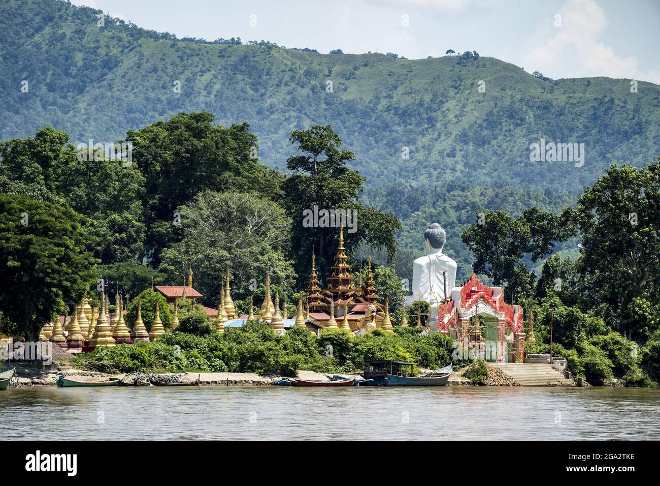 Vista da dietro di un Buddha gigante accanto a pagode e stupa d'oro sull'isola di Shwe Paw e barche ormeggiate lungo il fiume Ayeyarwady (Irrawaddy) Foto Stock