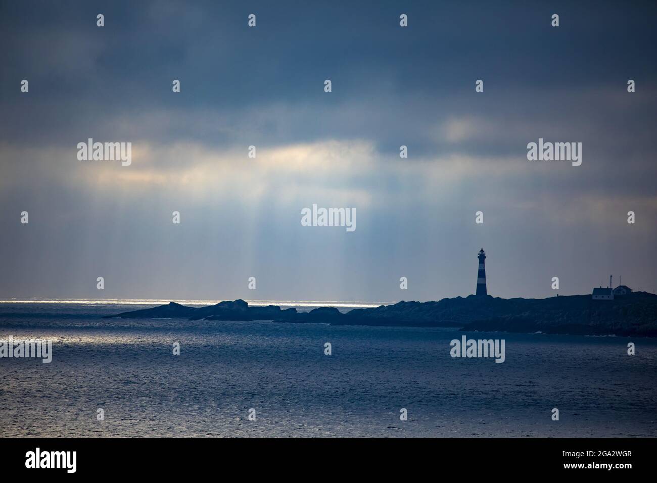 Faro di Hellisoy, un faro remoto su un'isola dei fiordi occidentali della Norvegia con raggi solari che si riflettono attraverso un cielo tempestoso; Hordaland, Norvegia Foto Stock