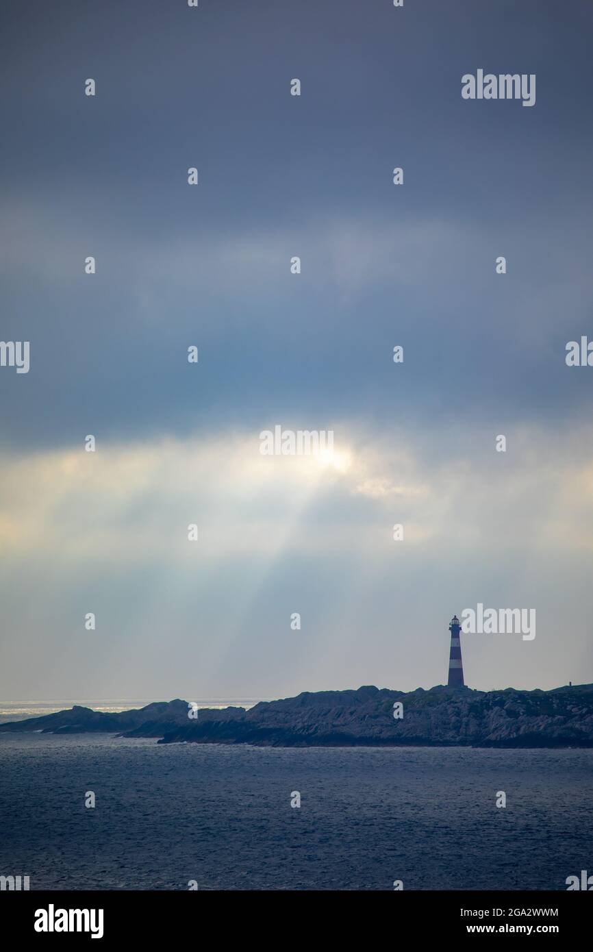 Faro di Hellisoy, un faro remoto su un'isola dei fiordi occidentali della Norvegia con raggi solari che si riflettono attraverso un cielo tempestoso; Hordaland, Norvegia Foto Stock