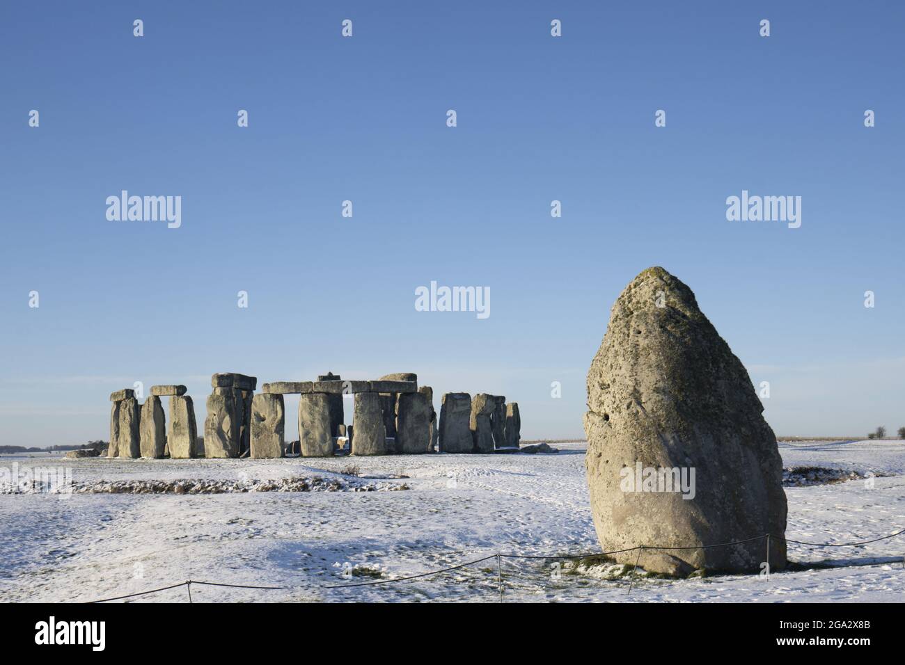 Stonehenge definito dalla neve di mattina presto con un cielo blu e la pietra di Heel fuori alla destra del cerchio di pietra; Wiltshire, Inghilterra, Regno Unito Foto Stock