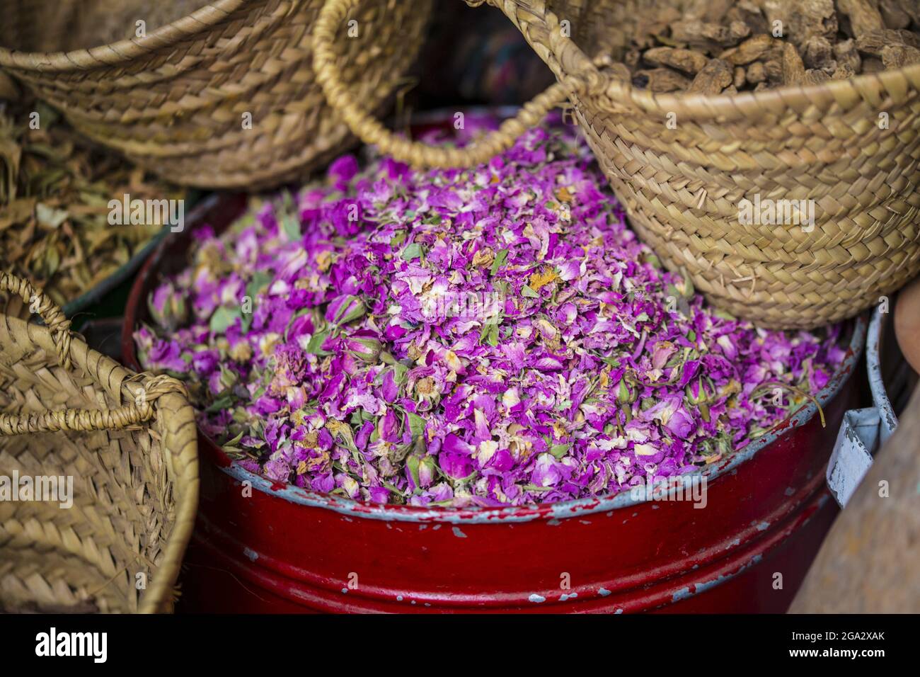 Primo piano del contenitore metallico con petali di rosa secchi e cesti di spezie in vendita nel souk delle spezie nella Medina di Marrakech Foto Stock