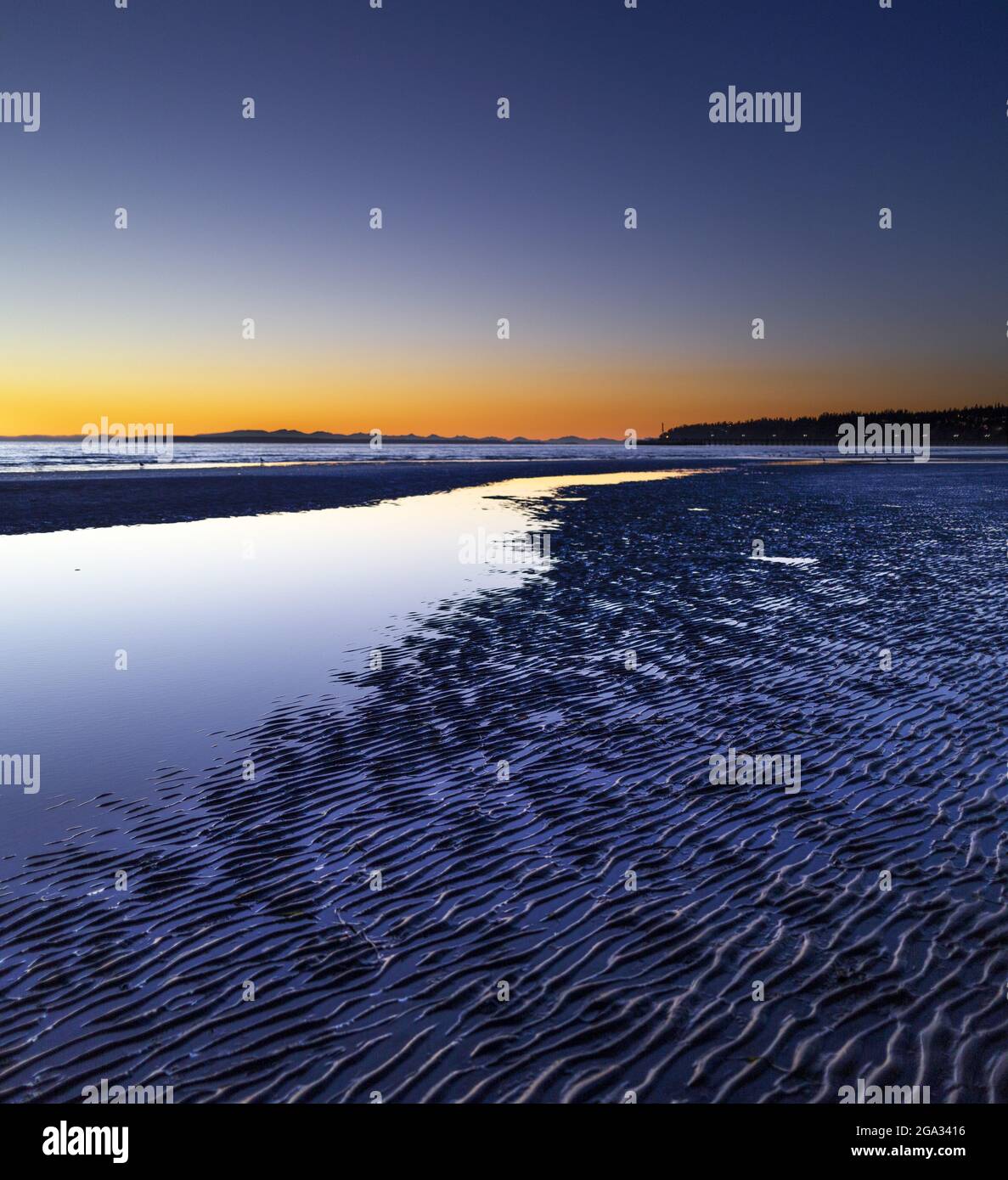 Sabbia ondulata, piscine maree e bassa marea con un orizzonte luminoso al tramonto; White Rock, British Columbia, Canada Foto Stock