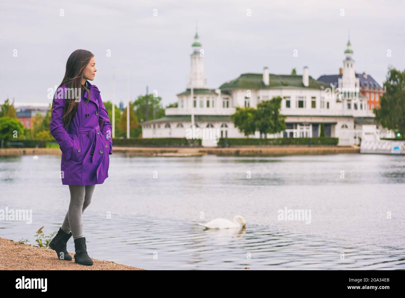 Donna in trench viola che cammina nel parco cittadino rilassandosi durante il fine settimana. Si gode la vista sul lago a Copenhagen, Danimarca. Attività primaverile Foto Stock