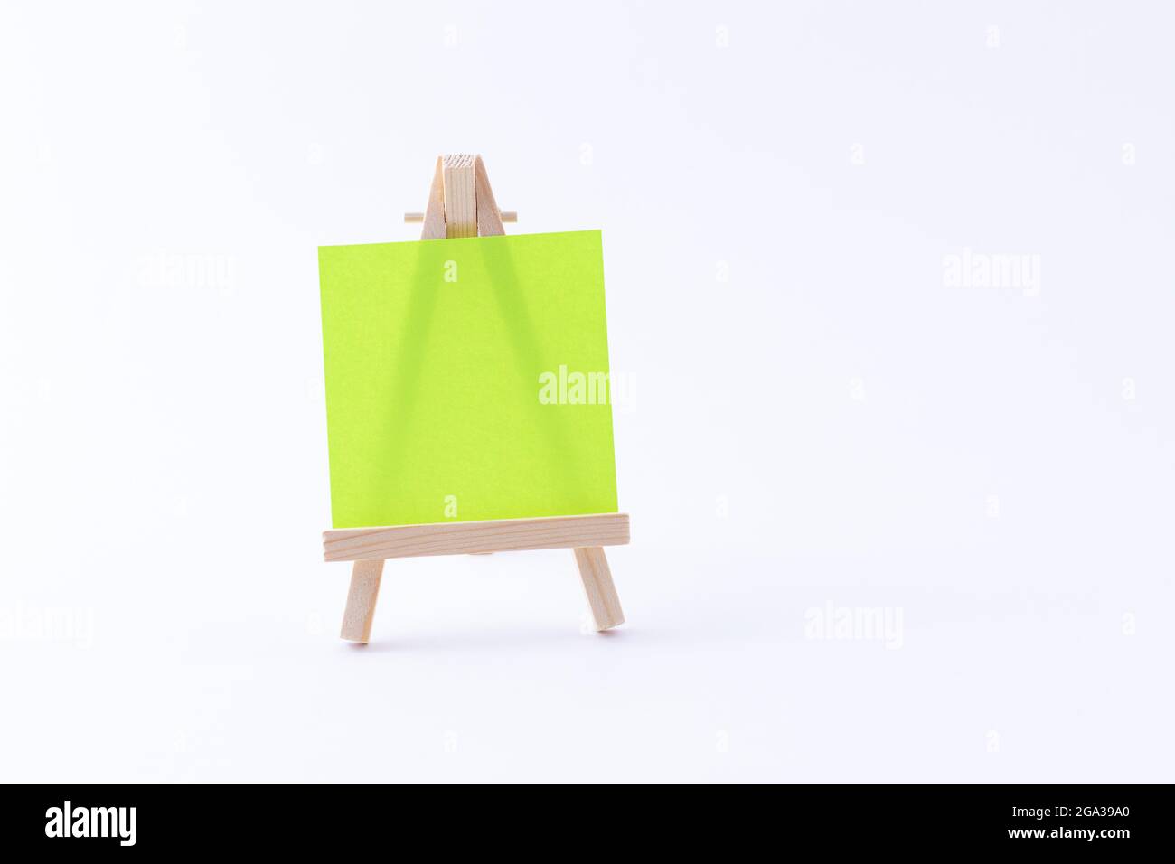 Easel in legno in miniatura con tela quadrata colorata vuota o carta Memo - Mockup. Mini supporto in legno con tavola da disegno pulita su sfondo bianco, spazio per la copia Foto Stock