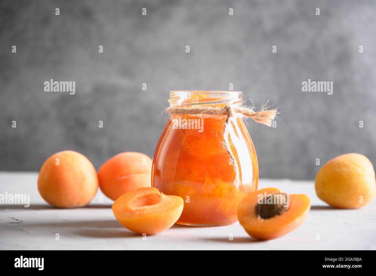 Marmellata fatta in casa di albicocche in vaso di vetro su fondo bianco della cucina. Raccolta estiva e cibo in scatola per l'inverno. Dessert gustoso. Primo piano. Foto Stock