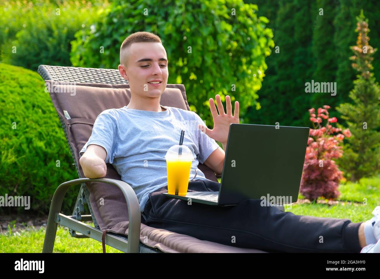 Uomo con braccio amputato beve un cocktail e parla con gli amici tramite il computer portatile Foto Stock