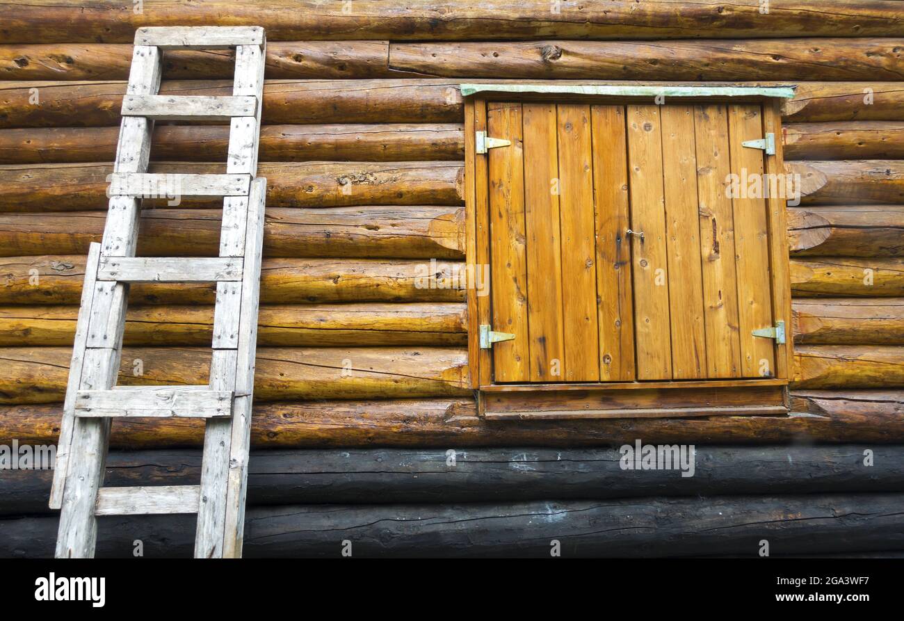 Vista frontale della cabina in legno rustico d'epoca con finestra chiusa e scala in legno sulla parete esterna in tessuto Foto Stock