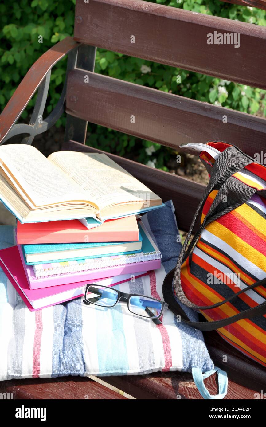 Libri, occhiali e borsa su panca all'aperto Foto Stock