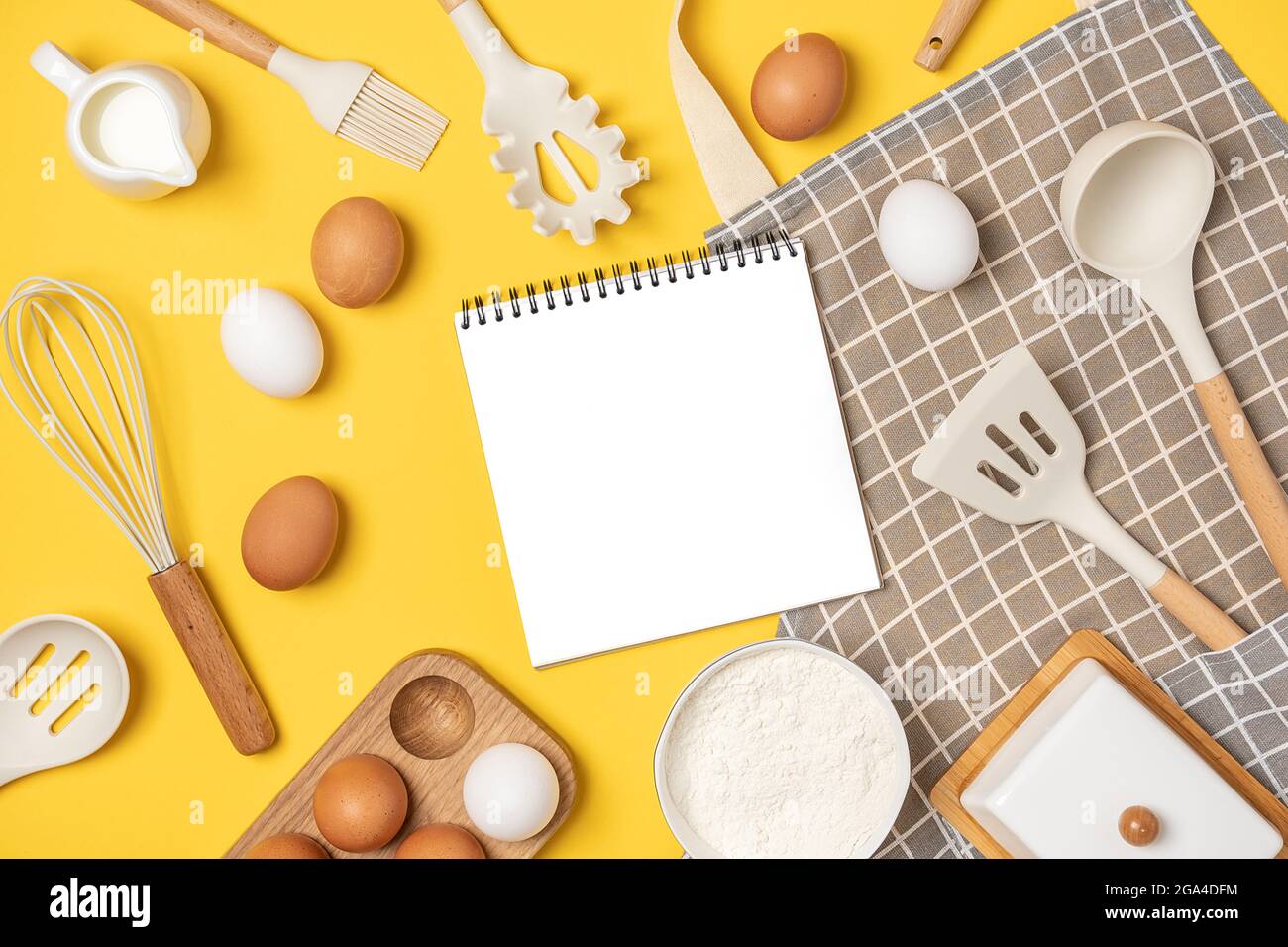 Ingredienti da forno, utensili da cucina e taccuino aperto su sfondo giallo. Modello per cucinare ricette o il vostro disegno. Vista dall'alto: Mockup a giacitura piatta. Foto Stock