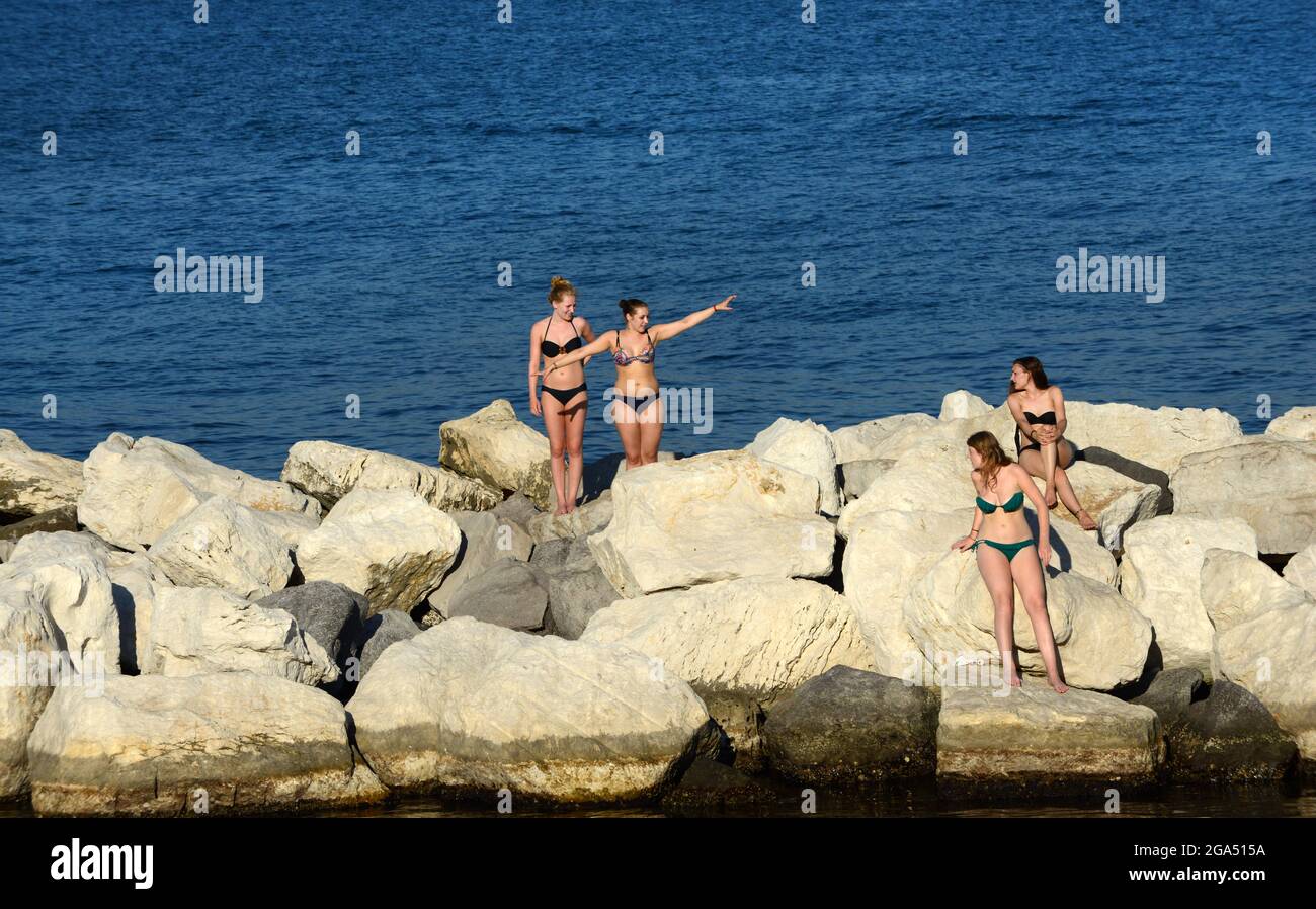 Un gruppo di giovani donne italiane che prendono il sole sui frangitori d'onda dei Giardini del Molosiglio di Napoli. Foto Stock
