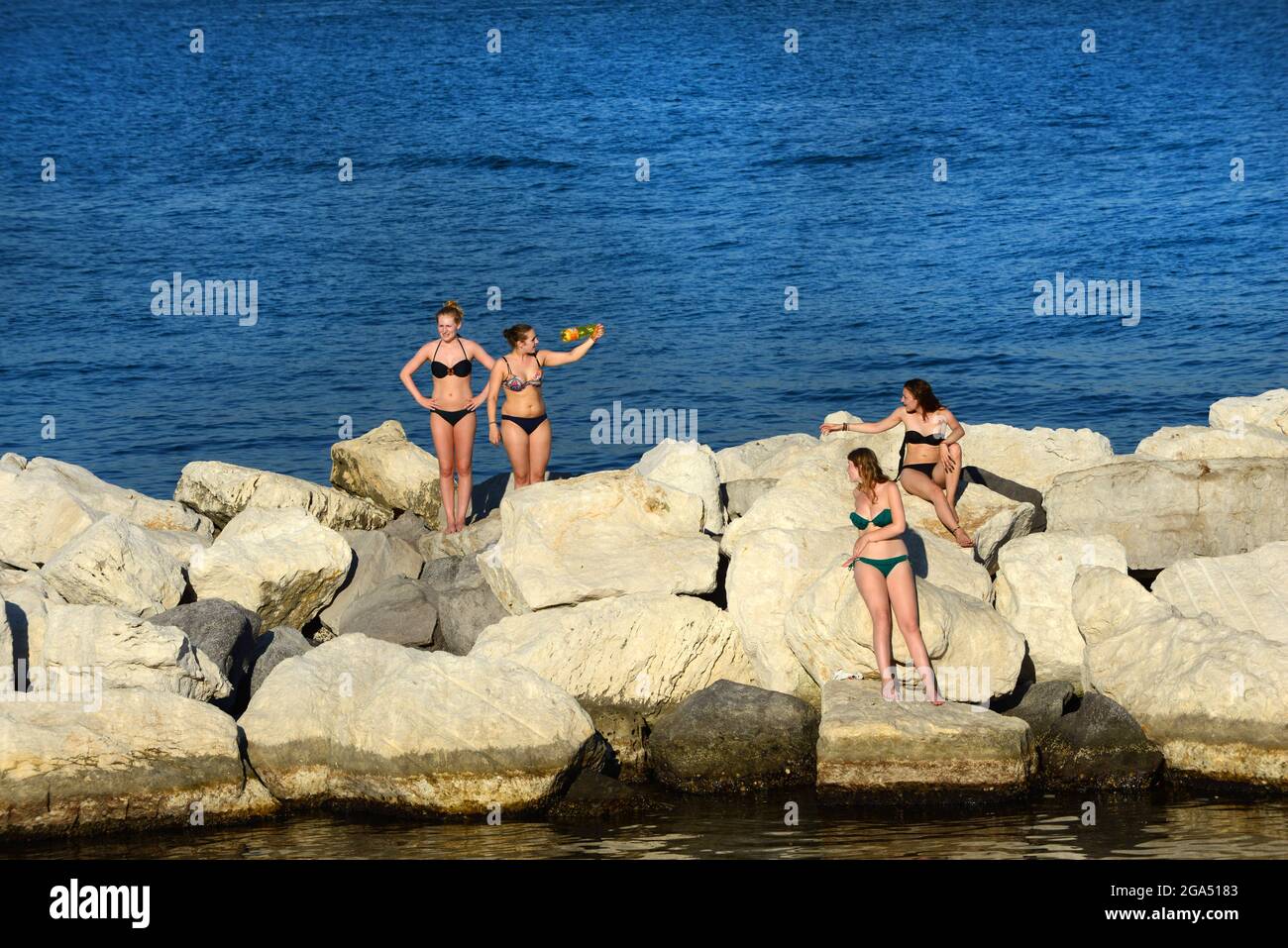 Un gruppo di giovani donne italiane che prendono il sole sui frangitori d'onda dei Giardini del Molosiglio di Napoli. Foto Stock