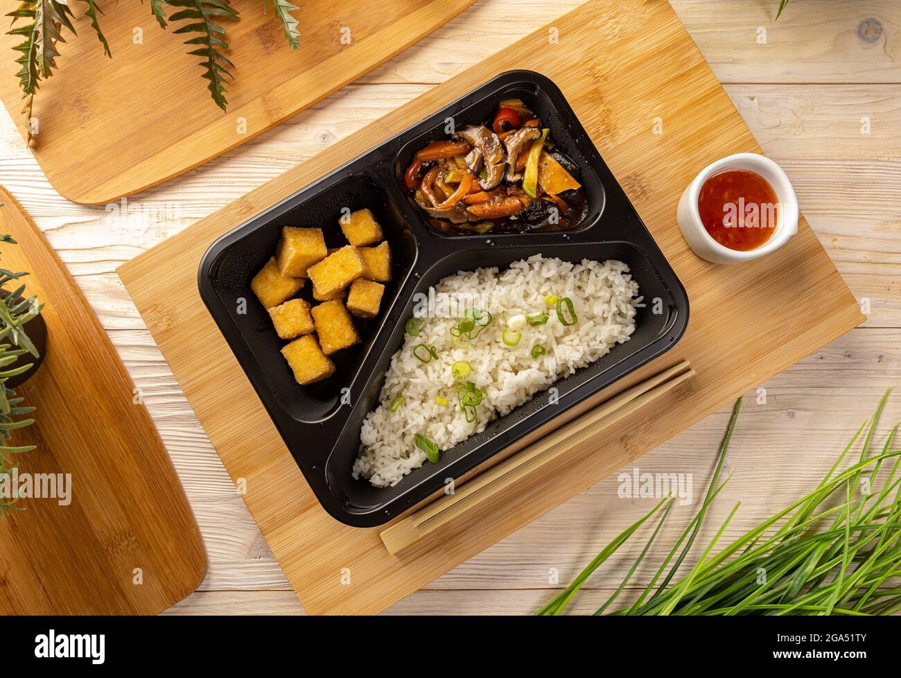 Piatto di riso con tofu e stufato di verdure in scatola da take-out su tagliere di bambù Foto Stock