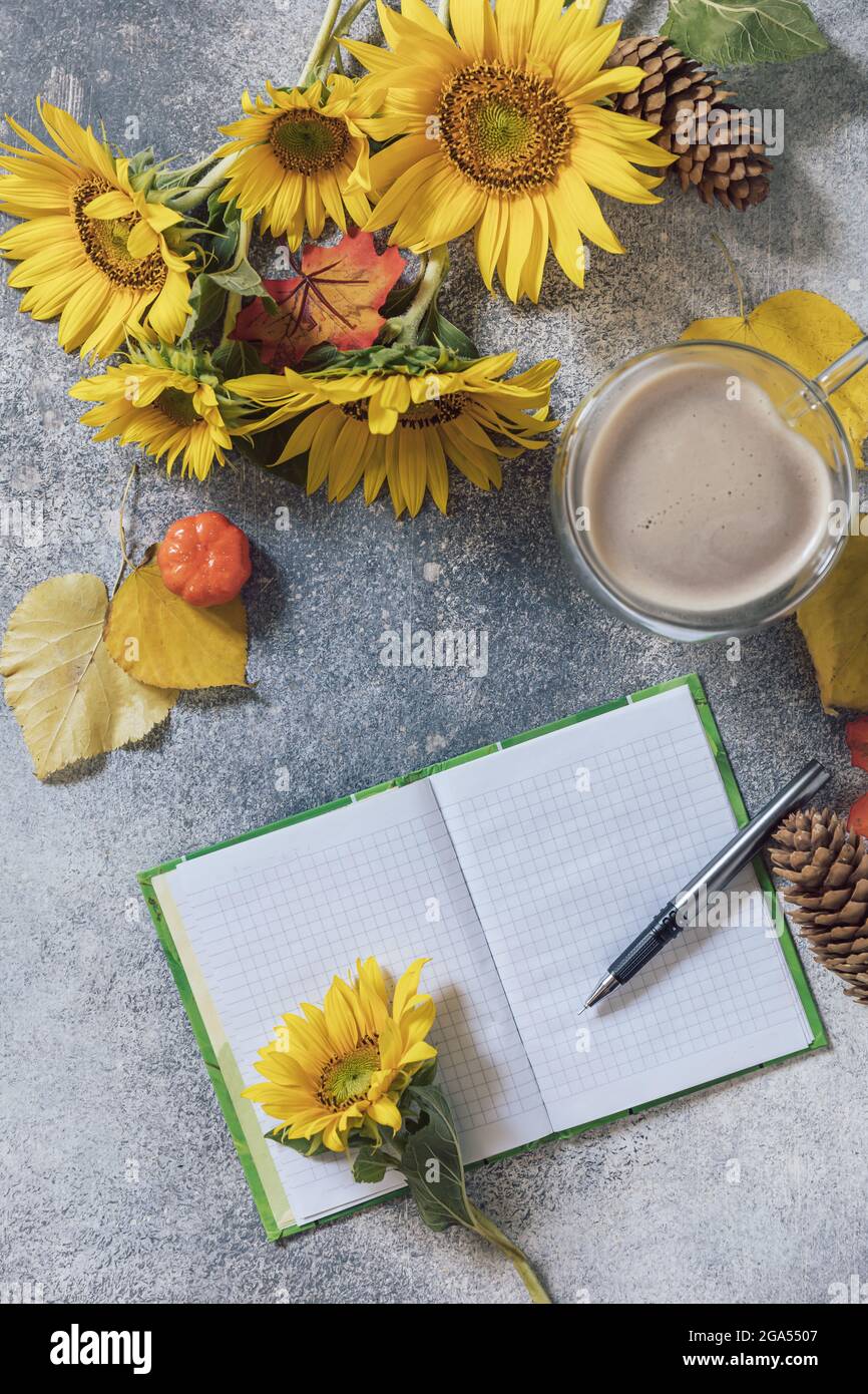 Buongiorno. Concetto di elenco attività. Un bouquet di grandi girasoli, una tazza di caffè e un taccuino vuoto su un tavolo di pietra. Vista dall'alto sfondo piatto. Foto Stock
