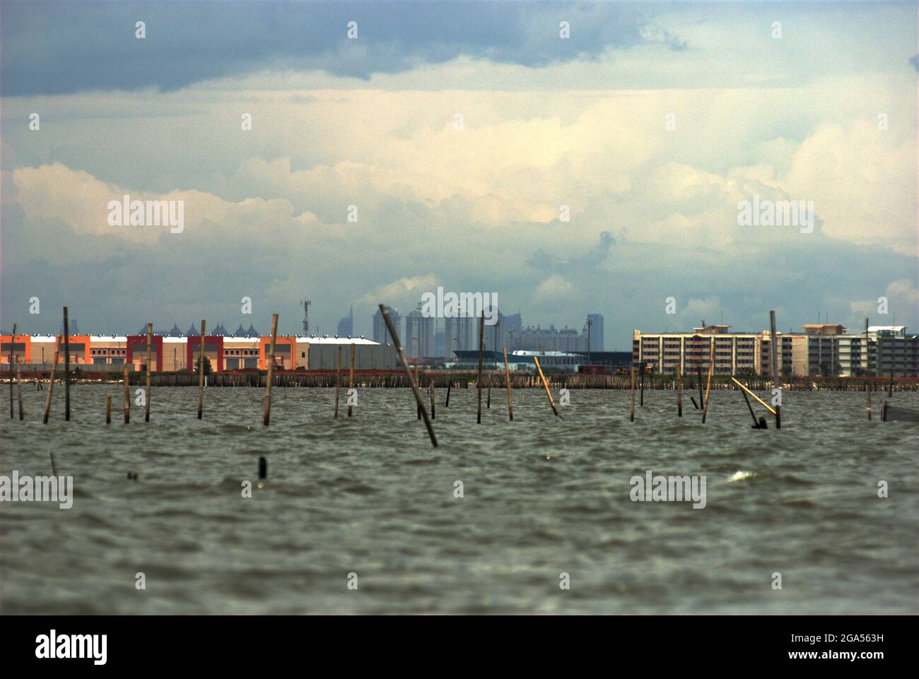 Una vista dalle acque costiere di Bekasi appena prima del confine con Giacarta. Una nuova area commerciale chiamata Marunda Makmur sull'estuario del canale delle inondazioni di Giacarta (a sinistra) e nuovi edifici piatti nel villaggio di Marunda a Giacarta (a destra) possono essere visti sullo sfondo di alcuni degli edifici torreggianti della capitale. Foto Stock