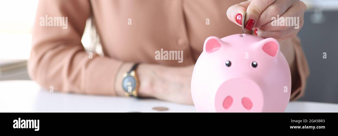 Mano di donna che mette la moneta nel guardaroba rosa della banca del piggy Foto Stock