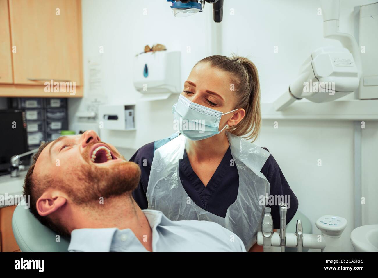 Paziente di sesso maschile caucasico seduto in sedia mentre i denti sono puliti da igienista orale femminile Foto Stock