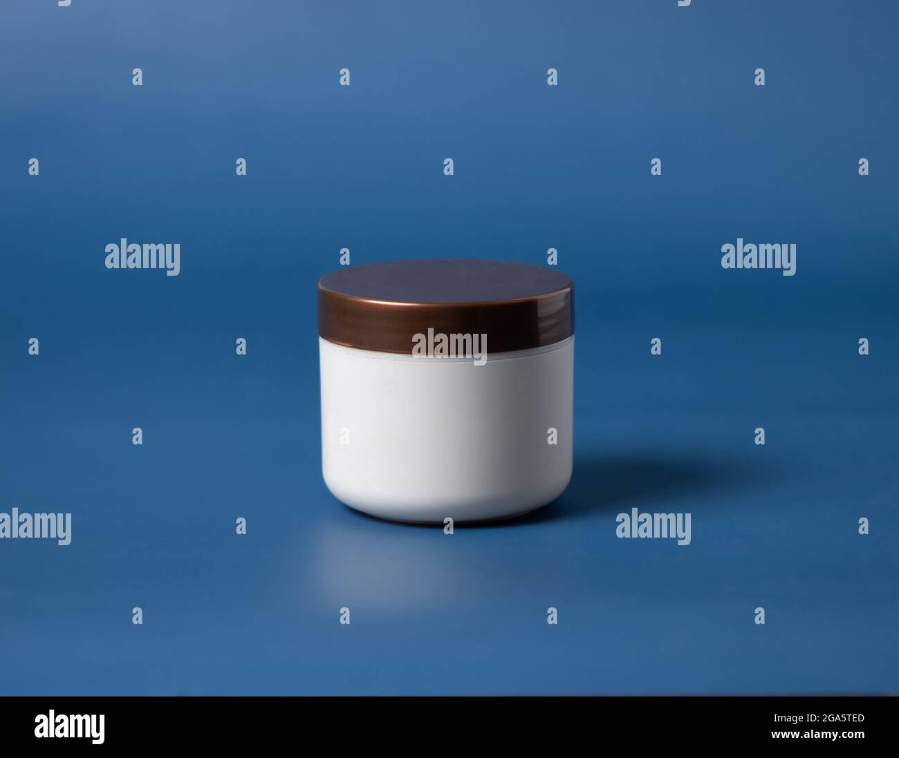 Vaso bianco panna con coperchio marrone su sfondo blu da vicino. Crema cosmetica può mockup Foto Stock