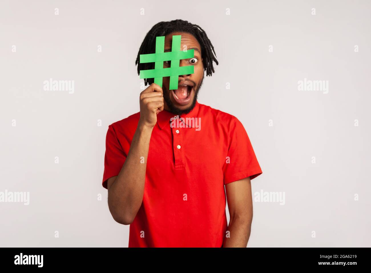 Ragazzo con Dreadlock indossando una T-shirt casual rossa, coprendo il viso con il simbolo hashtag social media, raccomandando di seguire contenuti alla moda, blog. IND Foto Stock