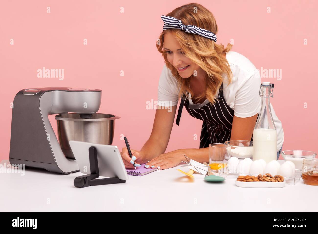 Giovane adulto concentrato femmina prepararsi a fare panetteria, scrivere nuova ricetta da internet, utilizzando tablet digitale, la preparazione di torte. studi interni Foto Stock