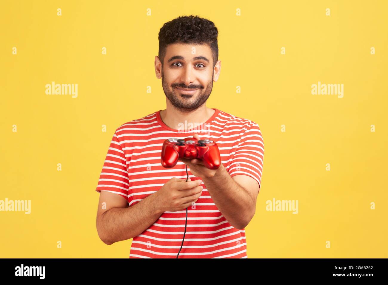 Generoso uomo bearded in t-shirt a righe che tiene in mano il joystick di gioco, suggerente di giocare il video gioco con lui, simulatore di realtà virtuale. Interno Foto Stock