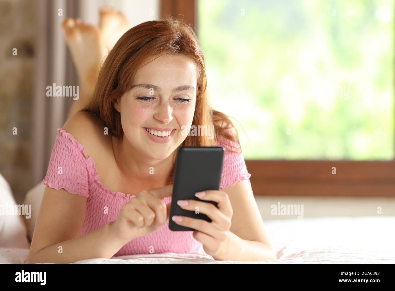Donna felice che usa lo smartphone che naviga contenuti online sul letto di casa Foto Stock