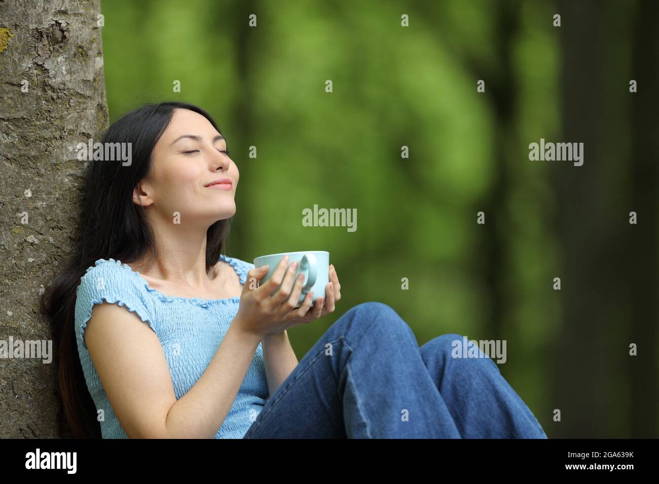 Donna asiatica felice bere caffè rilassante respirare aria fresca seduta in una foresta Foto Stock