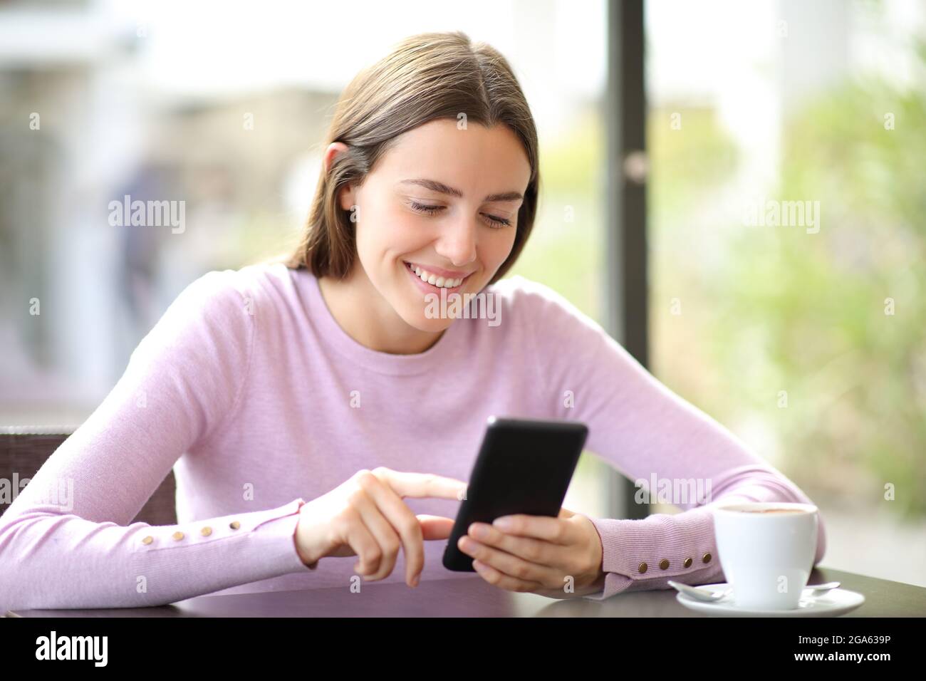 Donna felice che usa il telefono cellulare per controllare i contenuti online seduti in un bar Foto Stock