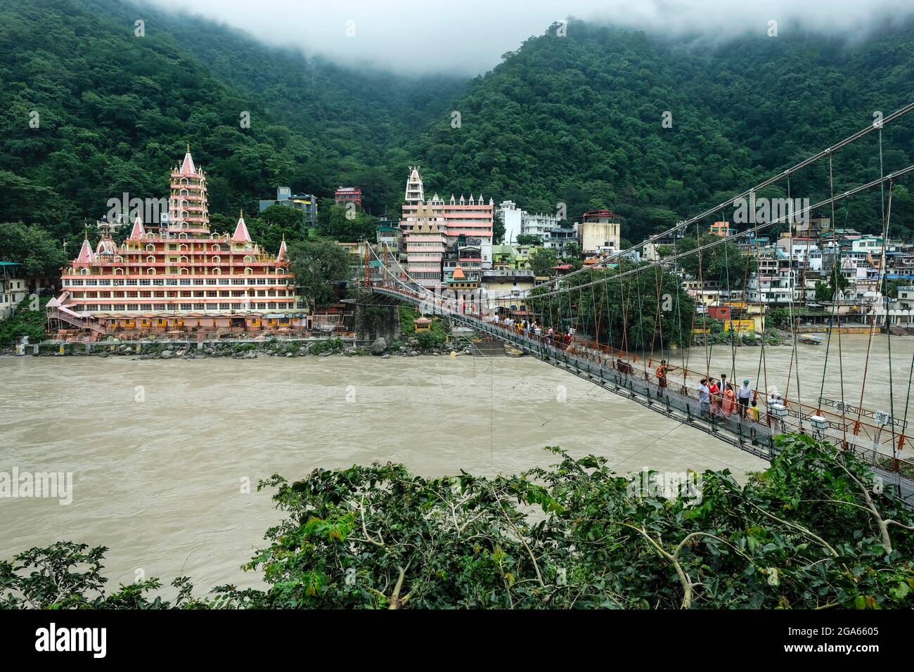 Rishikesh, India - 2021 luglio: Persone che passano dal ponte Lakshman Jhula accanto al tempio Swang Niwas a Rishikesh il 20 luglio 2021 a Uttarakhand, Foto Stock
