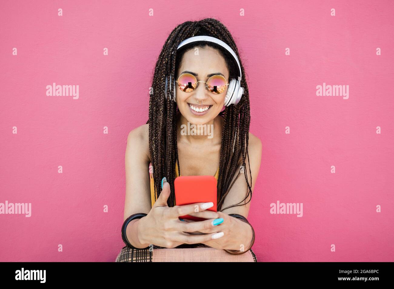 Happy bohemian influencer donna ascolto playlist musica con sfondo rosa - Focus on Face Foto Stock