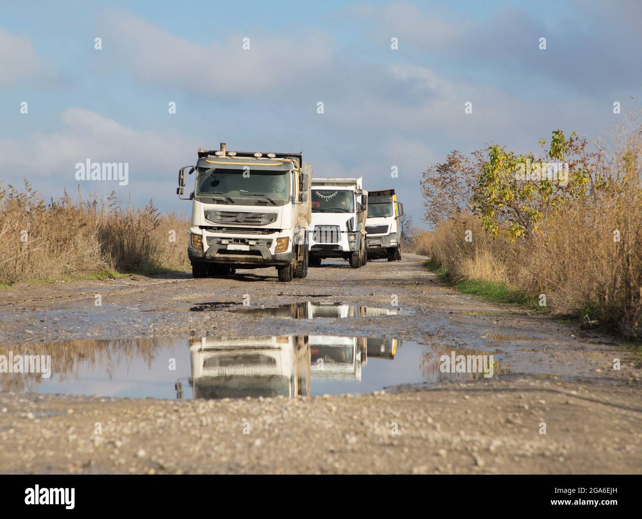 tre dumper guidano uno dopo l'altro su una strada sterrata dopo la pioggia. Il processo di trasporto e scarico del suolo su attrezzature da costruzione. Co Foto Stock