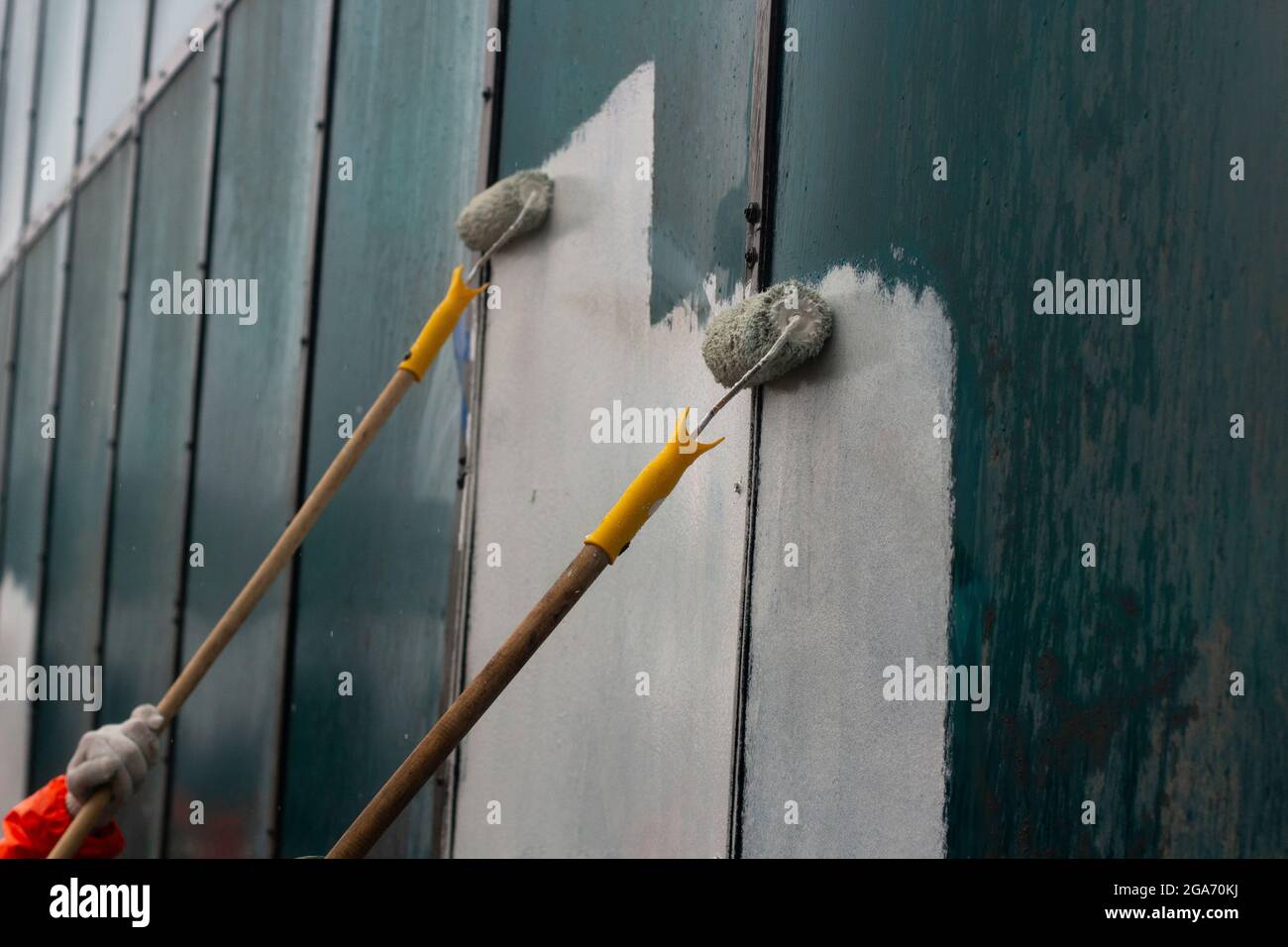 Dipinge i graffiti con un rullo. Il molare dipinge la parete con vernice bianca. Uno strumento per la verniciatura rapida delle superfici. Foto Stock