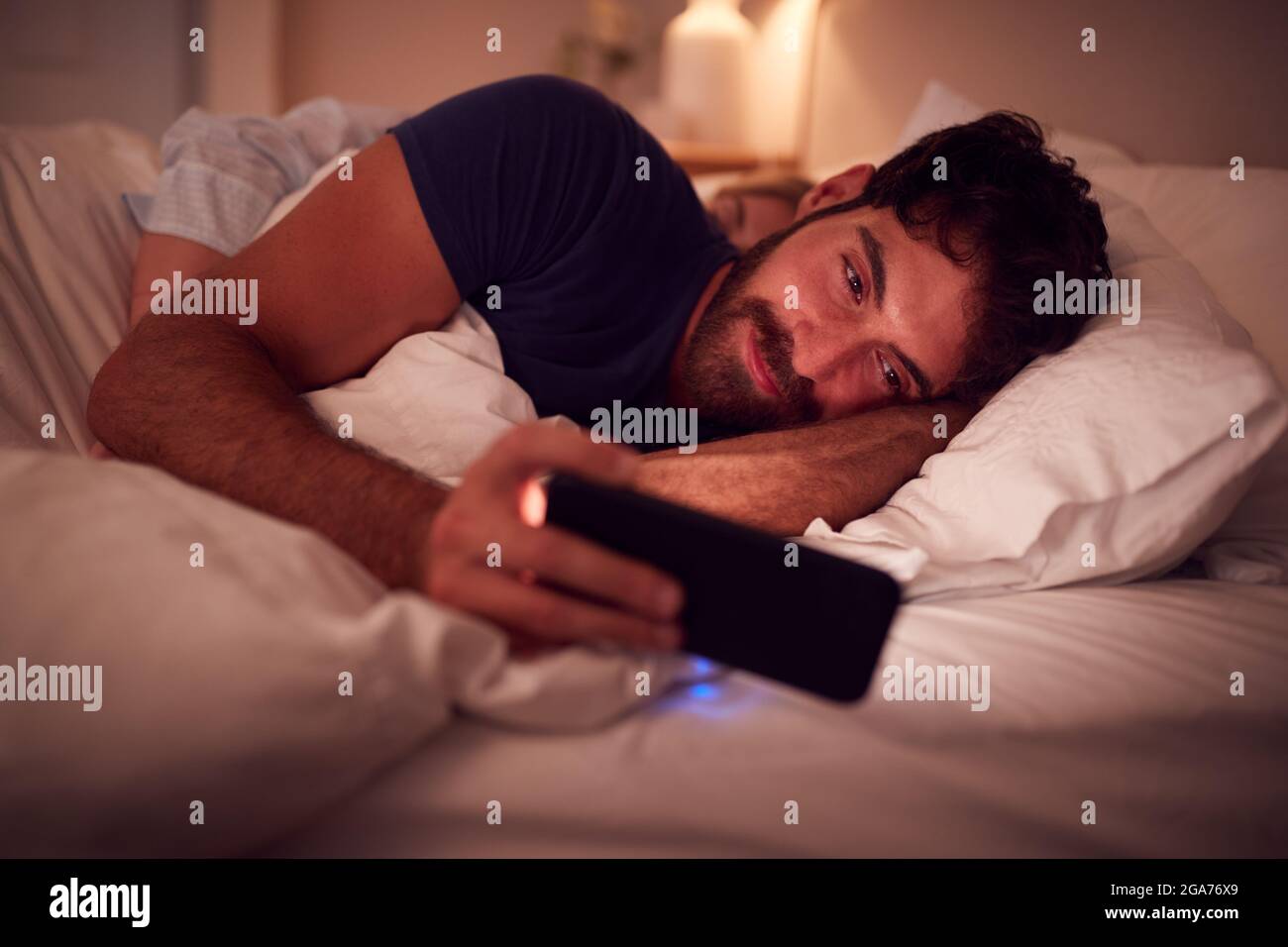 Coppia con l'uomo sdraiato a letto di notte guardando lo schermo del telefono cellulare Foto Stock