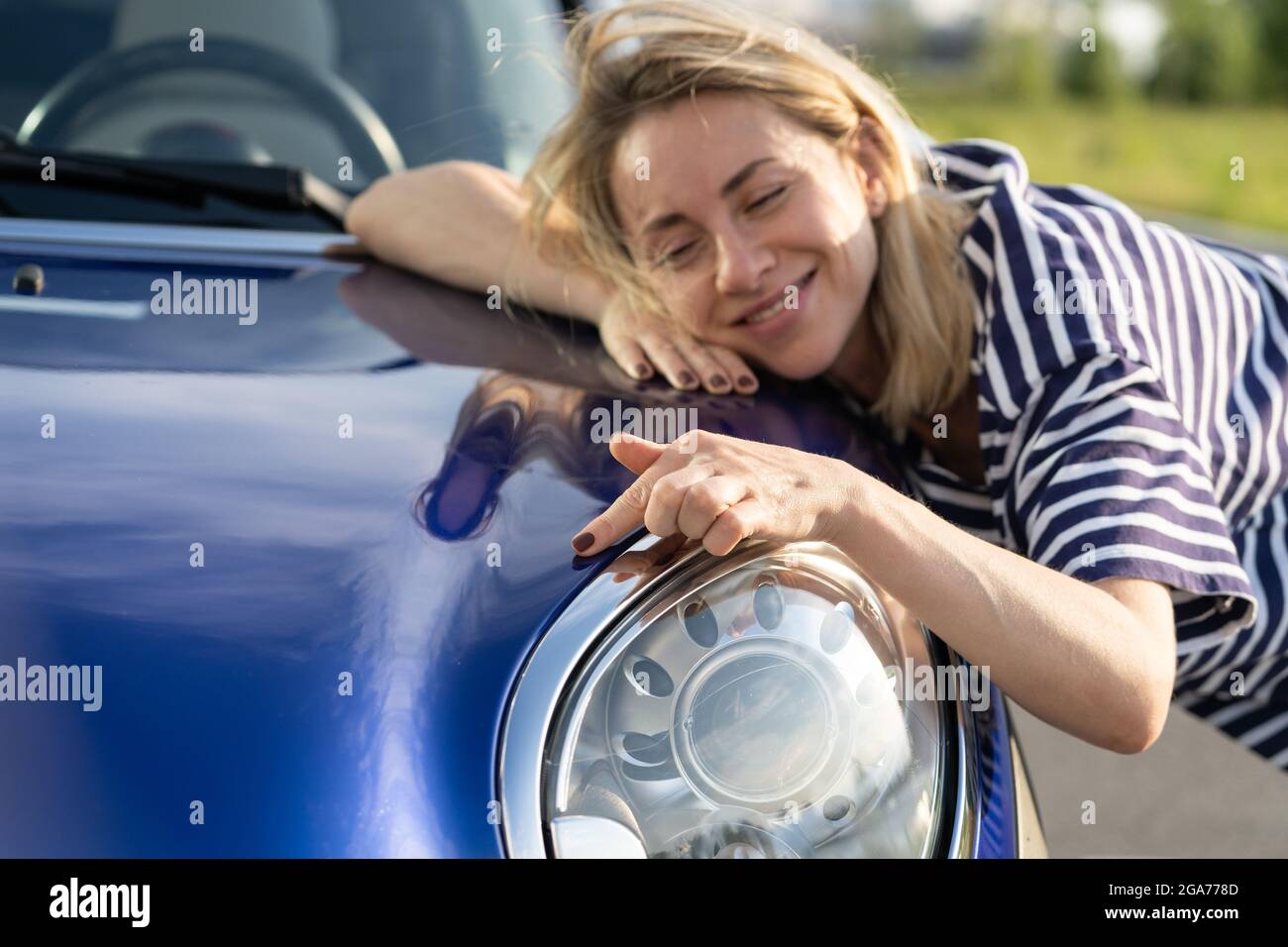 Conducente donna centrale che abbraccia il cofano dell'auto dopo i dettagli, la lucidatura. Pubblicità assicurazione auto Foto Stock