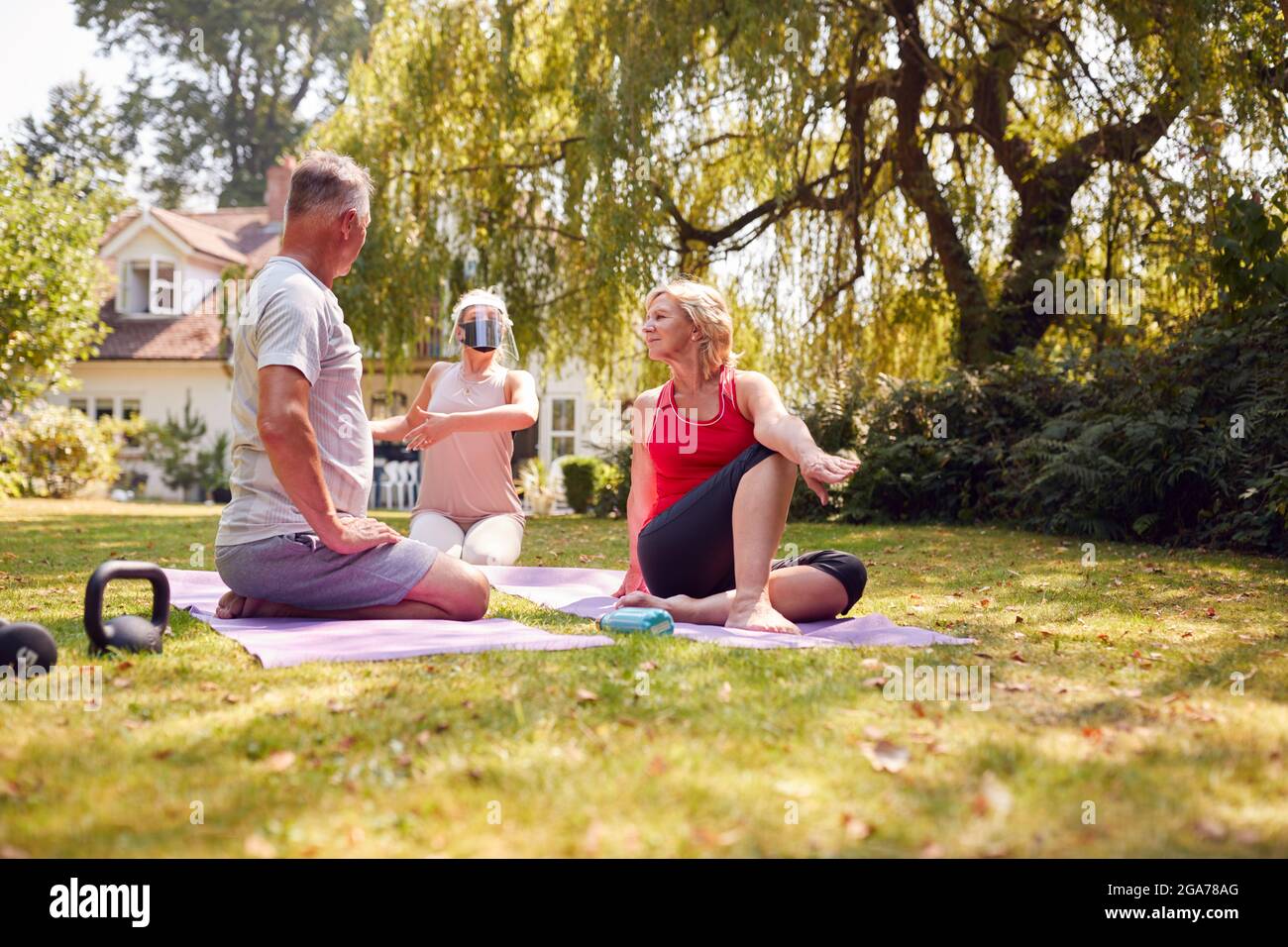 Coppia senior che partecipa a una lezione privata di yoga socialmente distanziata con insegnante a casa Foto Stock