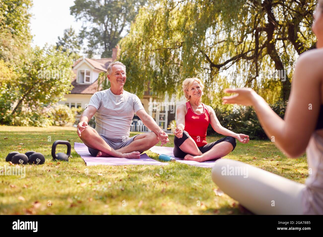 Coppia senior che partecipa alla lezione privata di yoga con insegnante in Giardino a casa Foto Stock