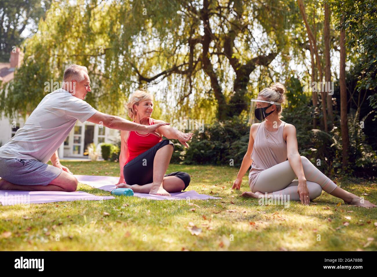 Coppia senior che partecipa a una lezione privata di yoga socialmente distanziata con insegnante a casa Foto Stock