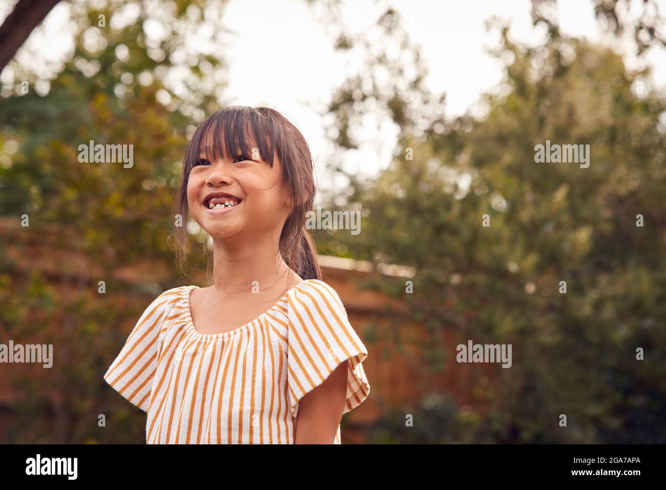 Ritratto di sorridente Asian Girl con i denti anteriori mancanti che si divertono in Giardino a casa Foto Stock