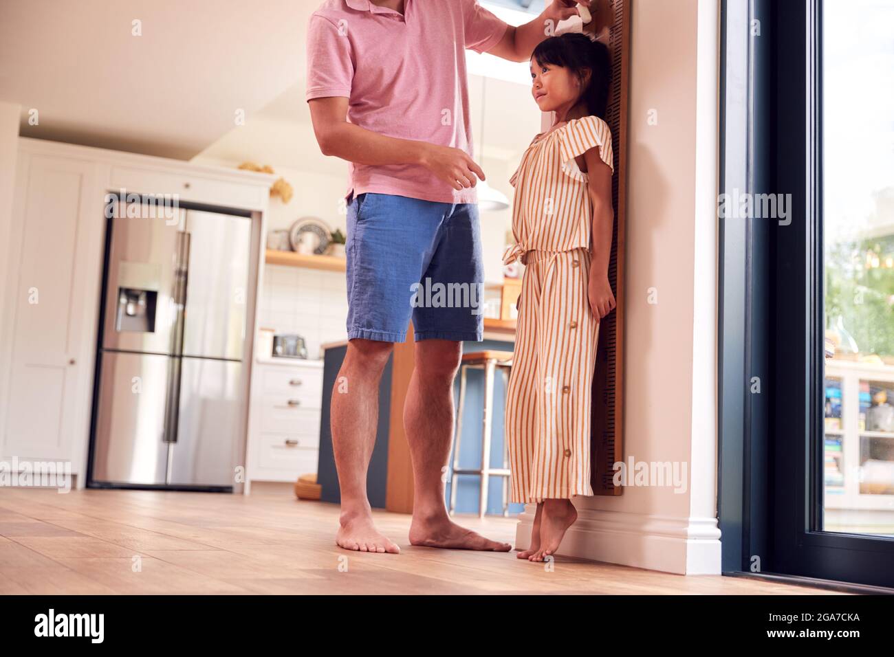Il padre asiatico misura la figlia sulla scala della parete a casa come lei sta sulle punte Foto Stock